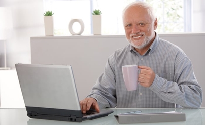 Hide the Pain Harold Meme, sitting at desk holding cup off coffee while using laptop