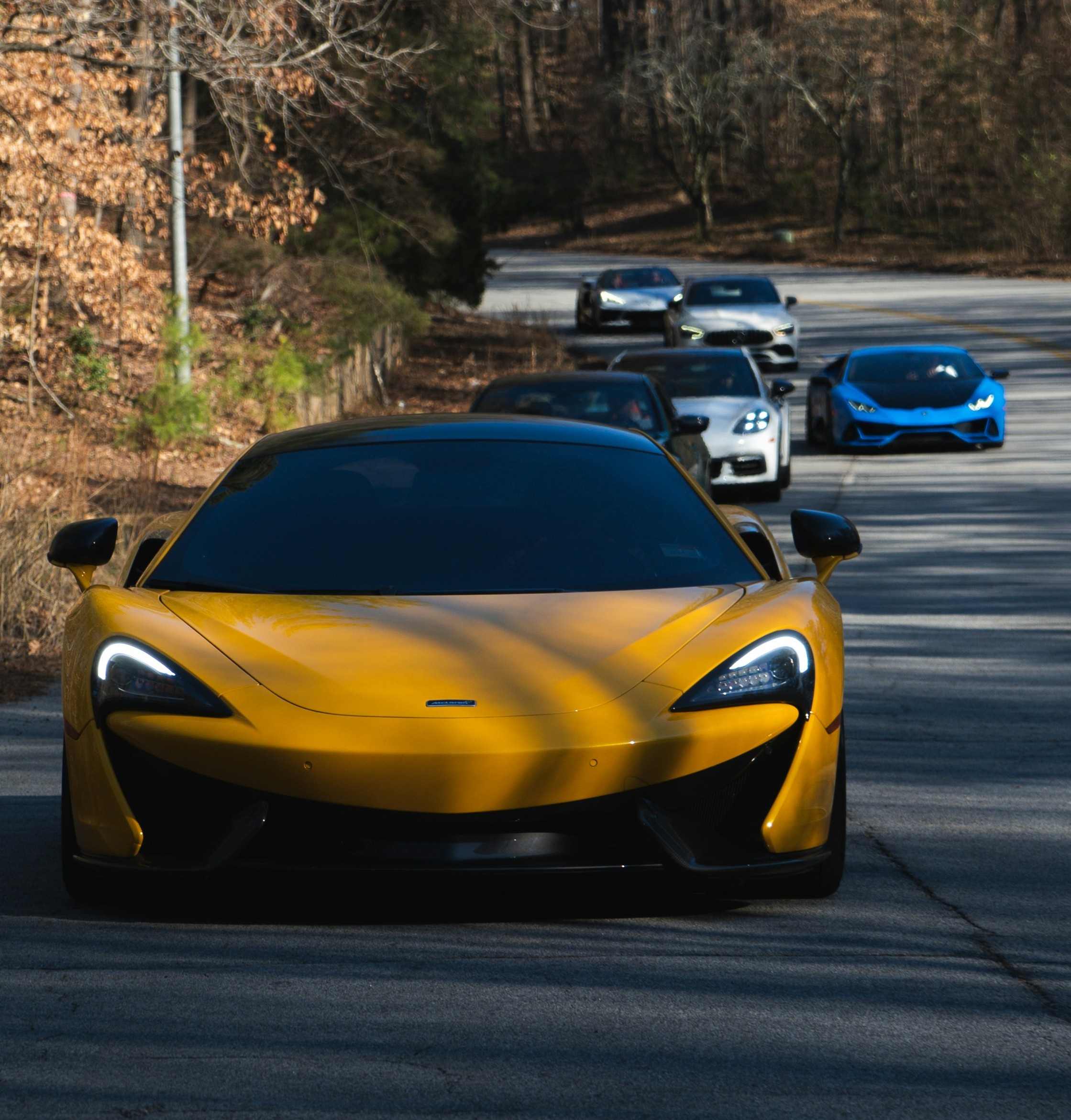 luxury cars driving down road in single file